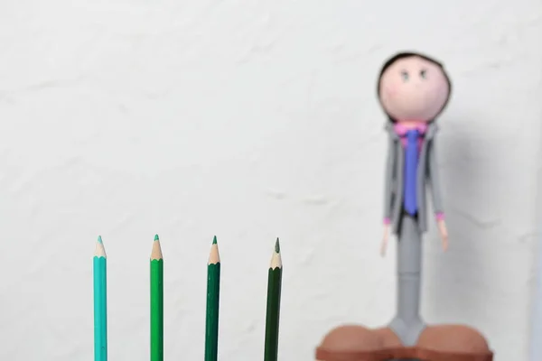 Color pencils in green shades. They are located vertically. Against the background of a white wall with decorative plaster. The figure of a schoolboy is out of focus. — Stock Photo, Image