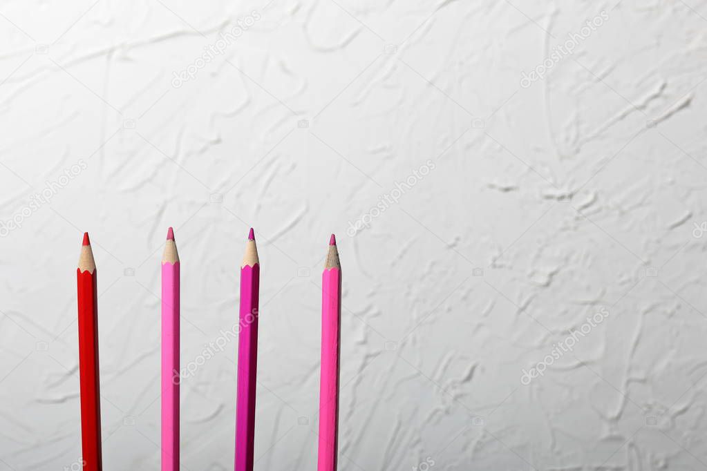 Colored pencils in coral and pink. They are located vertically. Against the background of a white wall with decorative plaster.