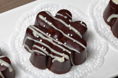 Çiçek şeklinde çikolatalı tatlı. Koyu çikolata kaplı. Beyaz çikolata ve sprinkles ile süslenmiş.