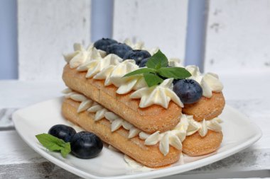 İtalyan savoyardi kurabiye ve krema yapılmış kek. Yaban mersini ve nane yaprakları ile dekore edilmiştir. Beyaz boyalı tahtalardan oluşan bir kutunun içinde duruyorlar..