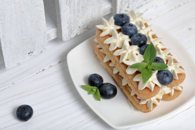 İtalyan savoyardi kurabiye ve krema yapılmış kek. Yaban mersini ve nane yaprakları ile dekore edilmiştir. Yakında beyaz boyalı ahşap tahtalar bir kutu.