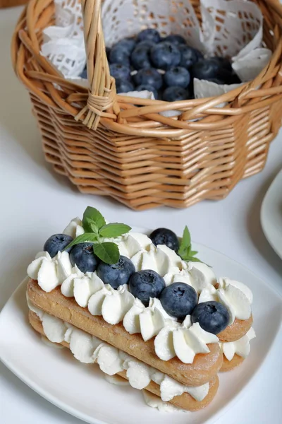 イタリアのサボヤードクッキーとクリームから作られたケーキ。ブルーベリーとミントの葉で飾られています。新鮮なブルーベリーは、ウィッカーバスケットに収集されます. — ストック写真