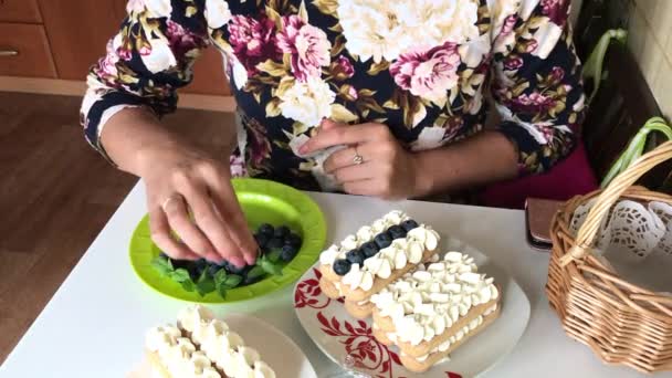 女性はミントの葉でケーキを飾ります サヴォイアルディクッキーとクリーム層の層はブルーベリーで飾られています — ストック動画
