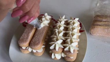 Bir kadın savoiardi kurabiyeleri üzerine krem uygular. Pasta poşeti kullanarak. Çiçek şeklinde.