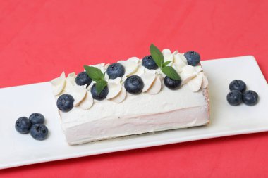 Sünger kek krema ile kaplanmış ve kurutulmuş yaban mersini ve taze nane yaprakları ile süslenmiş. Mercan renginin arka planına karşı.