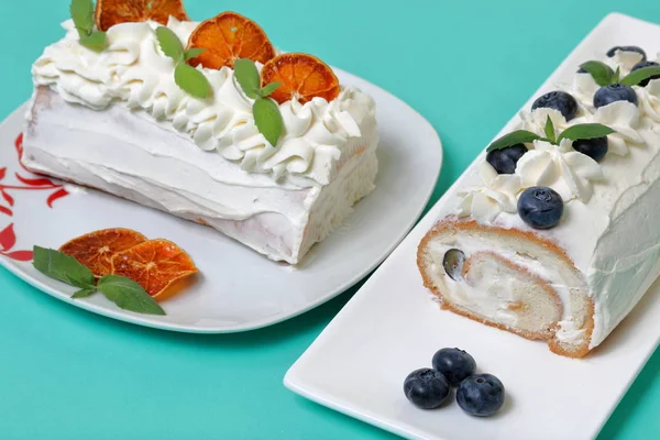 Bolo de esponja revestido com creme e decorado com mirtilos secos e folhas de hortelã fresca. Também as partes secas de cor-de-laranja. Contra o fundo da cor da hortelã . — Fotografia de Stock