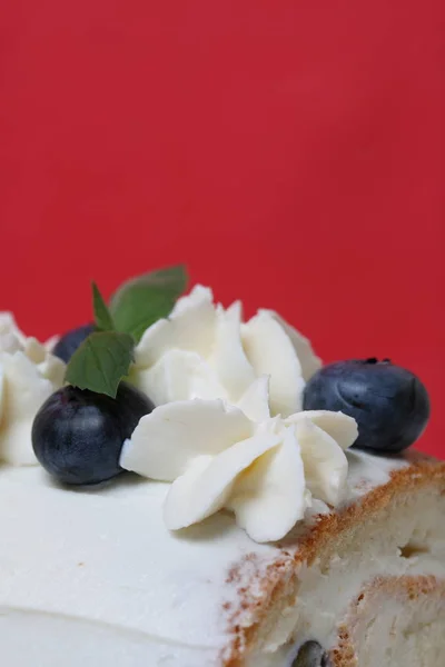 Sponge cake coated with cream and garnished with dried blueberries and fresh mint leaves. Against the background of coral color. — Stock Photo, Image