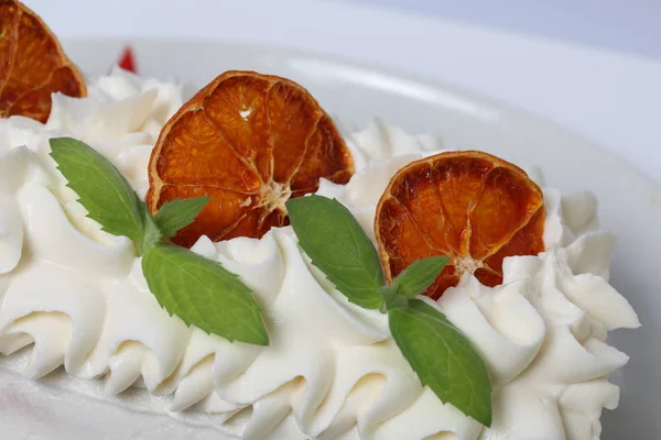 Κέικ κρέμας κρέμα με κρέμα και γαρνιρισμένο με αποξηραμένες φέτες πορτοκαλιού και φρέσκα φύλλα δυόσμου. — Φωτογραφία Αρχείου
