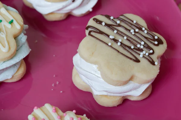 Marshmallow sandwiches from biscuit cookies and marshmallows. Decorated with white and black chocolate. With decorative sprinkles of different colors