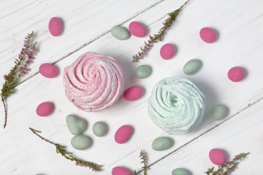 Pudra şekerinde pembe ve naneli marshmallow. Beyaz boyalı tahtalarda yatıyor. Yakındaki, farklı renklerde taşlar dekorasyon için dağınık. Heather dalları da görülebilir. Yukarıdan görüntüle.
