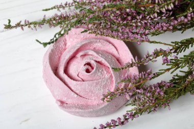 Pudra şekeri bir çiçek şeklinde pembe marshmallows. Beyaz boyalı tahtalarda yatıyor. Yakınlarda bir buket taze fundalık yer almaktadır. Yukarıdan görüntüle.