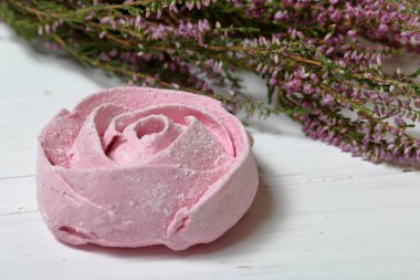 Pudra şekeri bir çiçek şeklinde pembe marshmallows. Beyaz boyalı tahtalarda yatıyor. Yakında taze fundalık bir buket yatıyor.