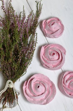 Pudra şekeri bir çiçek şeklinde pembe marshmallows. Beyaz boyalı tahtalarda yatıyor. Yakınlarda bir buket taze fundalık yer almaktadır. Yukarıdan görüntüle.