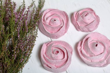 Pudra şekeri bir çiçek şeklinde pembe marshmallows. Beyaz boyalı tahtalarda yatıyor. Yakında taze fundalık bir buket yatıyor.