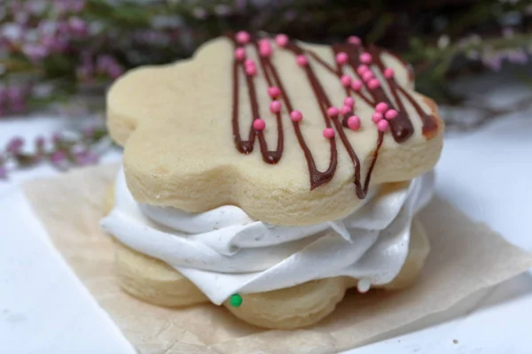 Marshmallow sandwich decorated with chocolate and decorative sprinkles. Nearby lies a bouquet of fresh heather. Close-up shot.