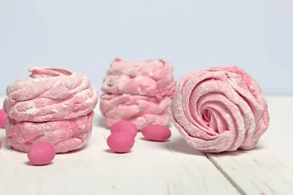 Růžovou Marshmallow v cukrové polevu. Leží na bílých malovaných deskách. Sousední růžové kameny jsou roztroušené k výzdobě. — Stock fotografie