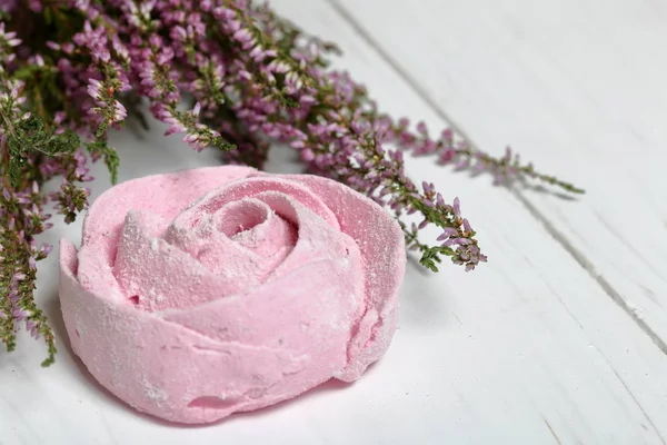 ピンクのマシュマロは、アイシングシュガーの花の形をしています。白い塗装されたボードの上に横たわっています。近くに新鮮なヘザーの花束があります. — ストック写真