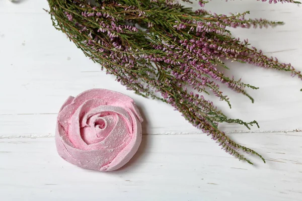 Los malvaviscos rosados en forma de la flor en el azúcar de guinda. Mentiras sobre tablas pintadas de blanco. Cerca se encuentra un ramo de brezo fresco. Vista desde arriba . — Foto de Stock