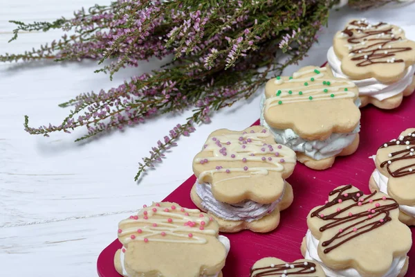 Marshmallow sandwich decorated with chocolate and decorative sprinkles. Set with decoration of different colors. Nearby lies a bouquet of fresh heather. — Stock Photo, Image