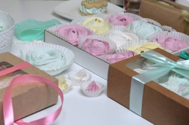 Marshmallows farklı renk ve şekillerde. Bazıları çiçek şeklinde. Hediye kutularına yığılmış. Yakındaki soyunma kutuları için renkli kurdeleler vardır.