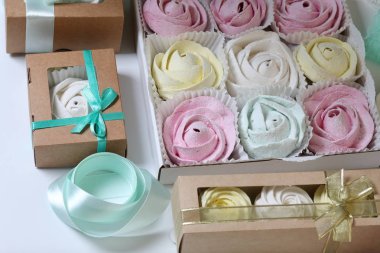 Marshmallows farklı renk ve şekillerde. Bazıları çiçek şeklinde. Hediye kutularına yığılmış. Yakındaki soyunma kutuları için renkli kurdeleler vardır.