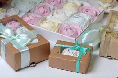 Marshmallows farklı renk ve şekillerde. Bazıları çiçek şeklinde. Hediye kutularına yığılmış. Yakındaki soyunma kutuları için renkli kurdeleler vardır.