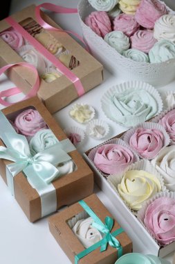 Marshmallows farklı renk ve şekillerde. Bazıları çiçek şeklinde. Hediye kutularına yığılmış. Yakındaki soyunma kutuları için renkli kurdeleler vardır.