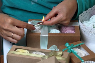 Kadın hediye kutularına farklı renklerde marshmallow koyar. Renkli kurdeleli bandaj kutuları. Bir yay üzerinde bir kurdele kravat ve yanan bir maç ile kenarı cauterize.