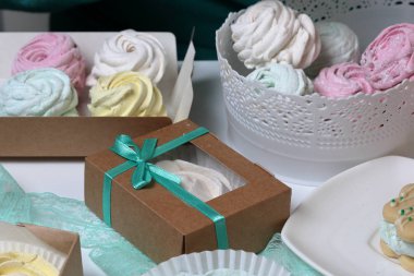 Marshmallows farklı renk ve şekillerde. Bazıları çiçek şeklinde. Hediye kutularına yığılmış. Yakındaki soyunma kutuları için renkli kurdeleler vardır.