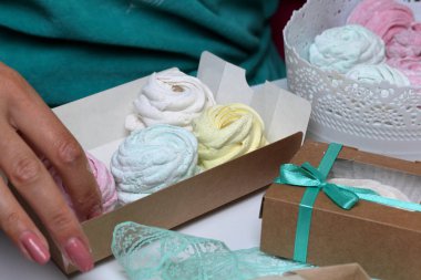 Kadın hediye kutularına farklı renklerde marshmallow koyar. Bandaj kutuları için yakındaki renkli kurdeleler.
