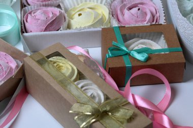 Marshmallows farklı renk ve şekillerde. Bazıları çiçek şeklinde. Hediye kutularına yığılmış. Yakındaki soyunma kutuları için renkli kurdeleler vardır.