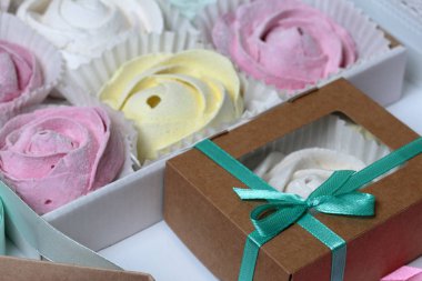 Marshmallows farklı renk ve şekillerde. Bazıları çiçek şeklinde. Hediye kutularına yığılmış. Yakındaki soyunma kutuları için renkli kurdeleler vardır.