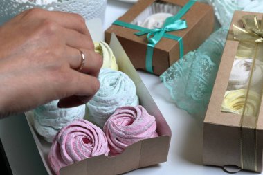 Kadın hediye kutularına farklı renklerde marshmallow koyar. Bandaj kutuları için yakındaki renkli kurdeleler.