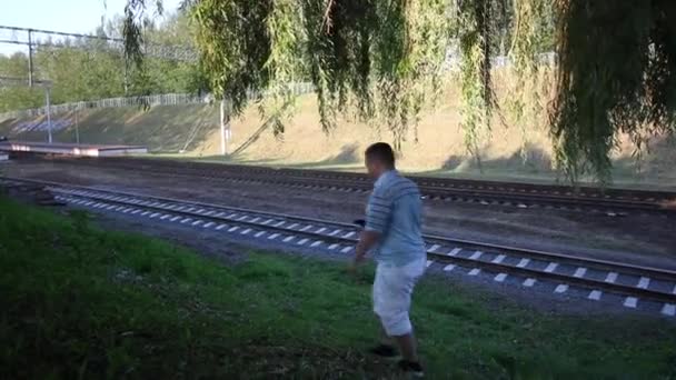 Un joven camina por las vías del tren. Pasa un tren de cercanías — Vídeo de stock