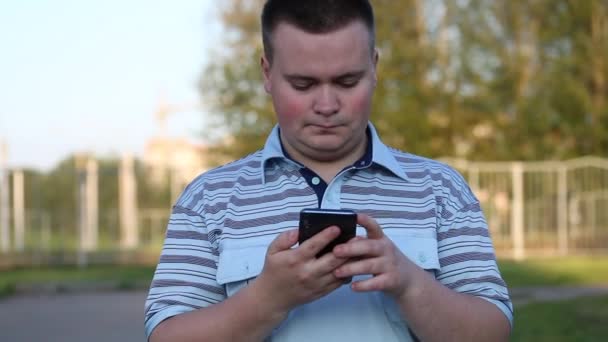 Ein junger Mann hält ein Smartphone in der Hand. arbeitet mit ihm, blickt nachdenklich auf den Bildschirm. — Stockvideo