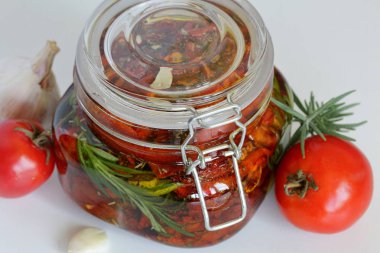 Bir kavanozda baharat ve sarımsak ile güneşte kurutulmuş domates. Biberiye, domates ve sarımsak yakınında.