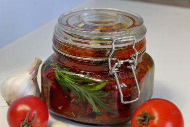 Bir kavanozda baharat ve sarımsak ile güneşte kurutulmuş domates. Biberiye, domates ve sarımsak yakınında.