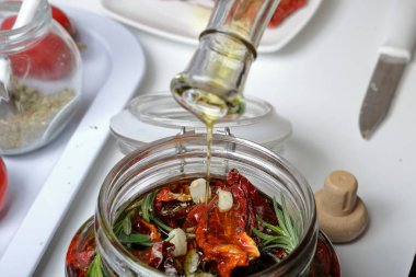 Bir kavanozda baharat ve sarımsak ile güneşte kurutulmuş domates. Kadın zeytinyağı ekler. Biberiye, domates ve sarımsak yakınında.