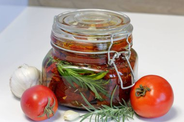 Bir kavanozda baharat ve sarımsak ile güneşte kurutulmuş domates. Biberiye, domates ve sarımsak yakınında.