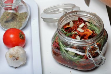 Bir kavanozda baharat ve sarımsak ile güneşte kurutulmuş domates. Biberiye, domates ve sarımsak yakınında.