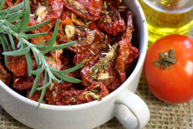 Bir tabakta baharat ve sarımsak ile güneşte kurutulmuş domates. Biberiye ve domatesyakınında.