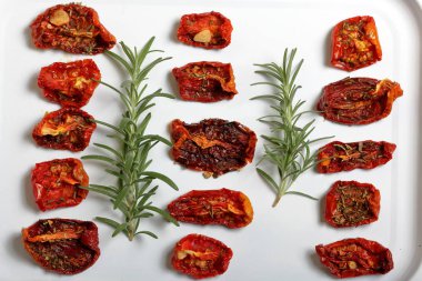 Hafif tepside baharat ve sarımsak ile güneşte kurutulmuş domates. Yakında taze biberiye yatıyor.