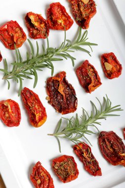 Hafif tepside baharat ve sarımsak ile güneşte kurutulmuş domates. Yakında taze biberiye yatıyor.