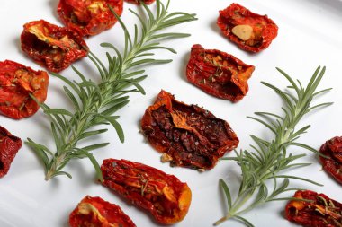 Hafif tepside baharat ve sarımsak ile güneşte kurutulmuş domates. Yakında taze biberiye yatıyor.