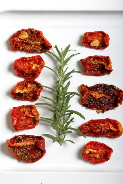 Hafif tepside baharat ve sarımsak ile güneşte kurutulmuş domates. Yakında taze biberiye yatıyor.