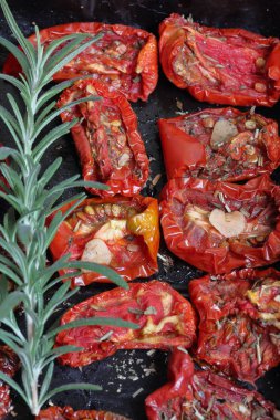 Bir fırın tepsisine baharat ve sarımsak ile güneşte kurutulmuş domates. Onların üzerinde taze biberiye yatıyor.