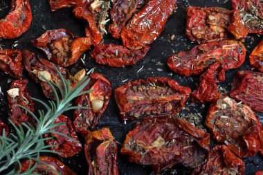 Bir fırın tepsisine baharat ve sarımsak ile güneşte kurutulmuş domates. Onların üzerinde taze biberiye yatıyor.