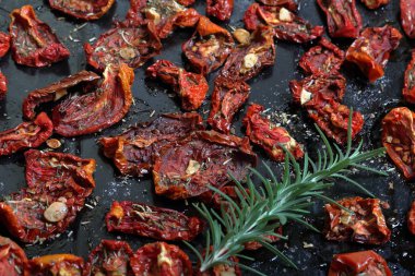 Bir fırın tepsisine baharat ve sarımsak ile güneşte kurutulmuş domates. Onların üzerinde taze biberiye yatıyor.