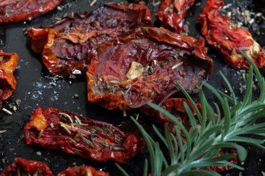 Bir fırın tepsisine baharat ve sarımsak ile güneşte kurutulmuş domates. Onların üzerinde taze biberiye yatıyor.