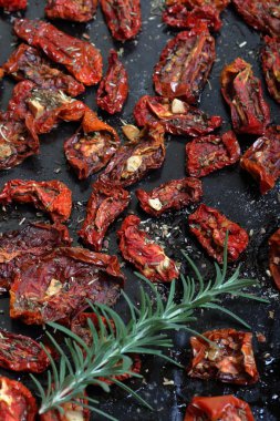 Bir fırın tepsisine baharat ve sarımsak ile güneşte kurutulmuş domates. Onların üzerinde taze biberiye yatıyor.